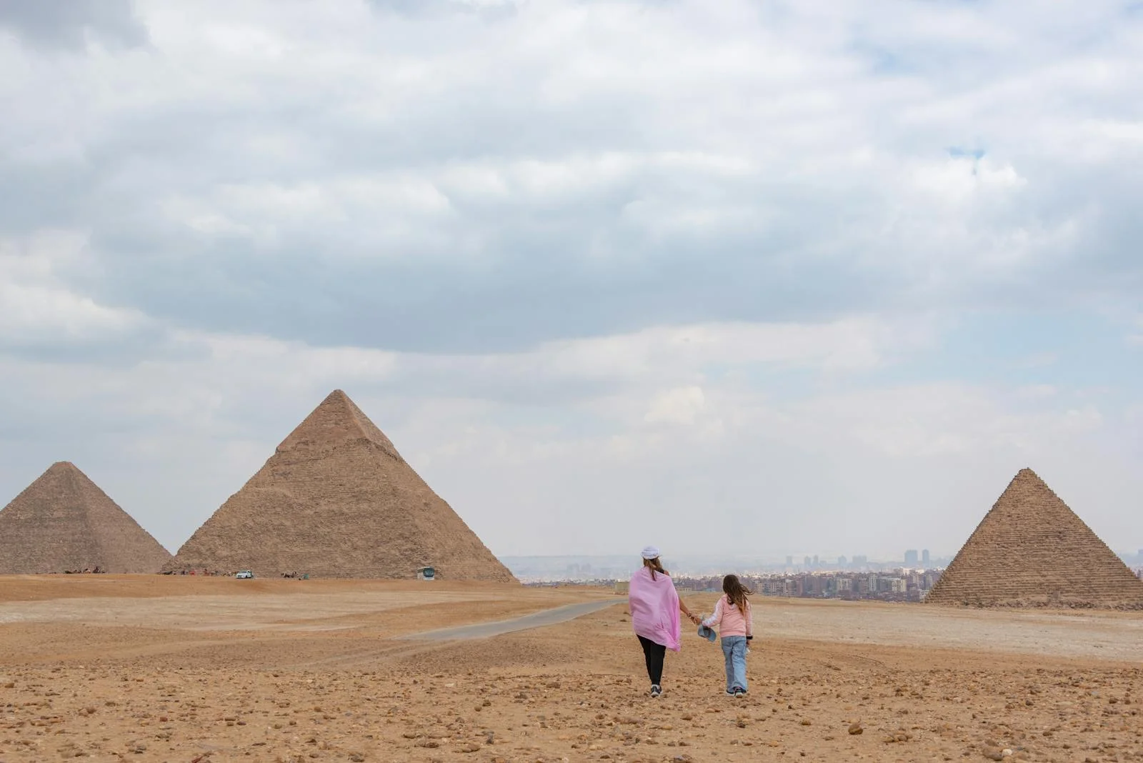 Unique Egyptian Family Traditions - A mother and daughter walk near the iconic Pyramids of Giza on a cloudy day.